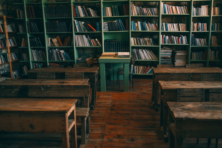A nostalgic view of an old classroom with wooden desks and bookshelves filled with books.